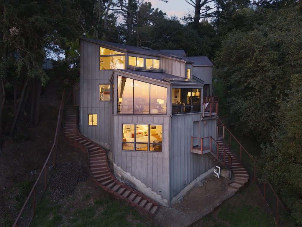A home between the trees in the Oakland hills at twilight with glowing windows.