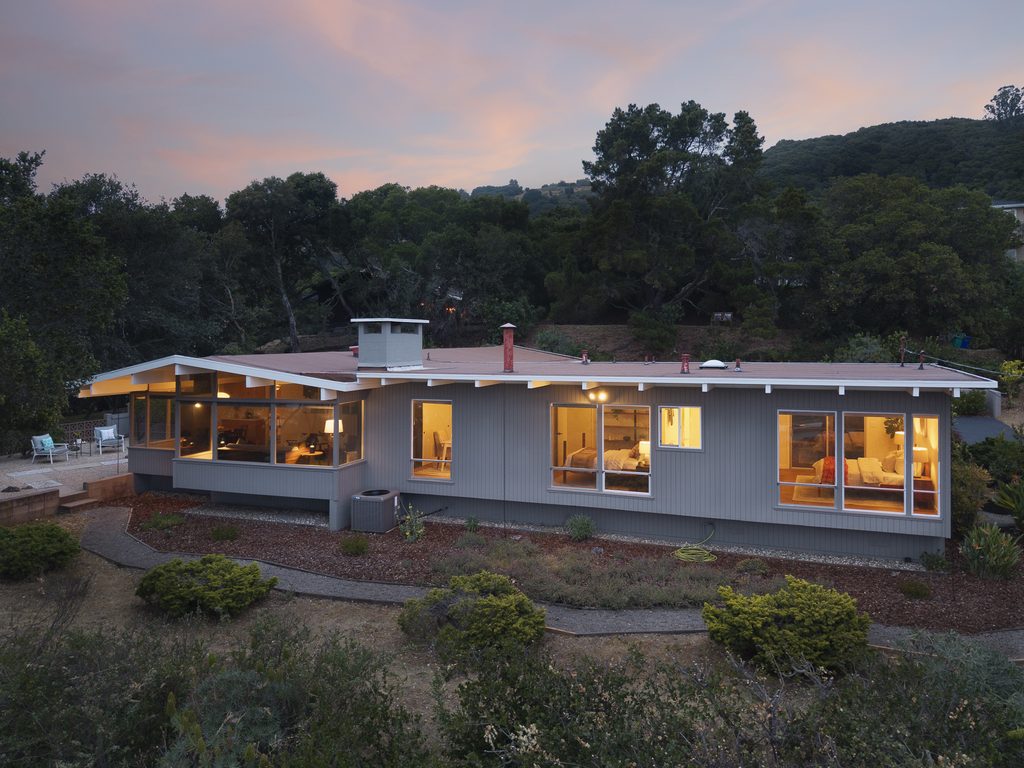 A mid-century modern house with glowing windows at twilight.