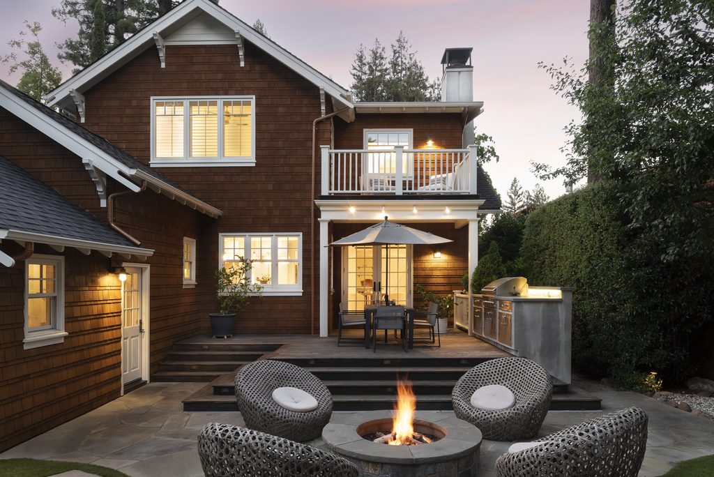 The backyard of a house at twilight with a conversation pit and a lit fire.